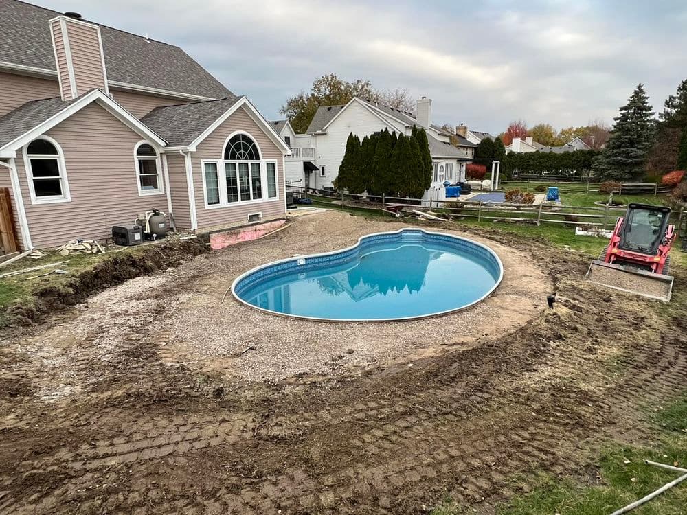 In-ground pool installation with gravel surround in residential backyard setting.
