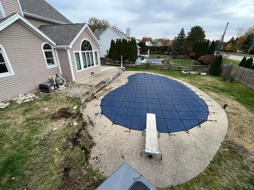 Pool cover installation on a residential patio with landscaping and cloudy sky.