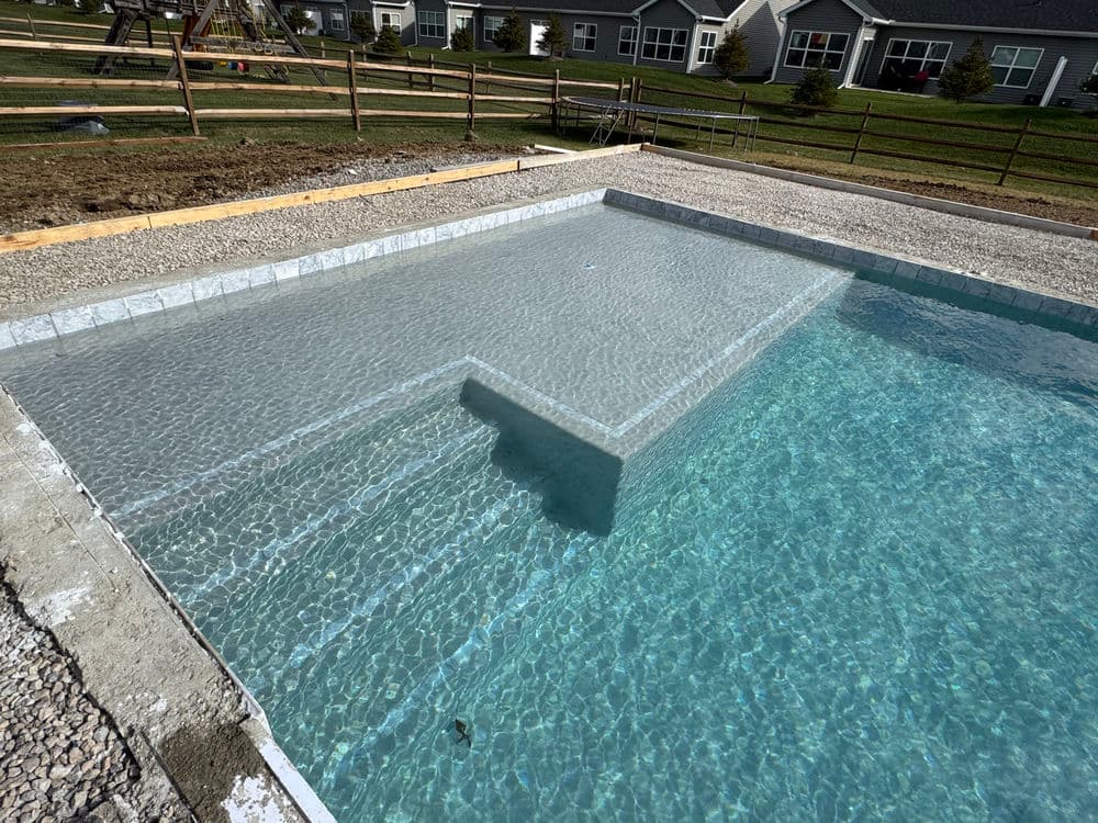 In-ground swimming pool with shallow step entry and clear water, surrounded by gravel and grass.