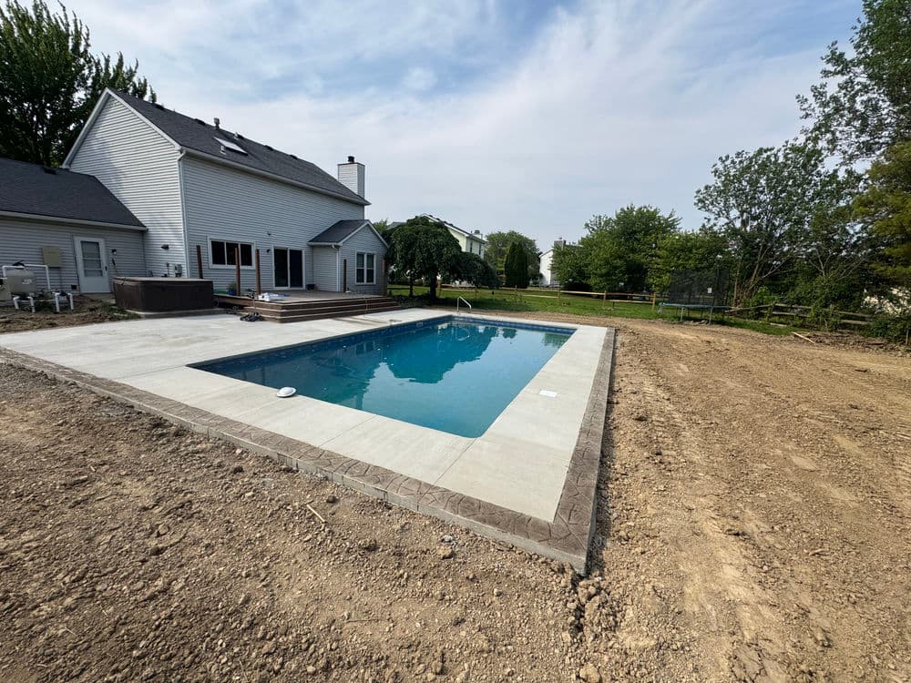 Newly built in-ground swimming pool with a patio in a residential backyard setting.