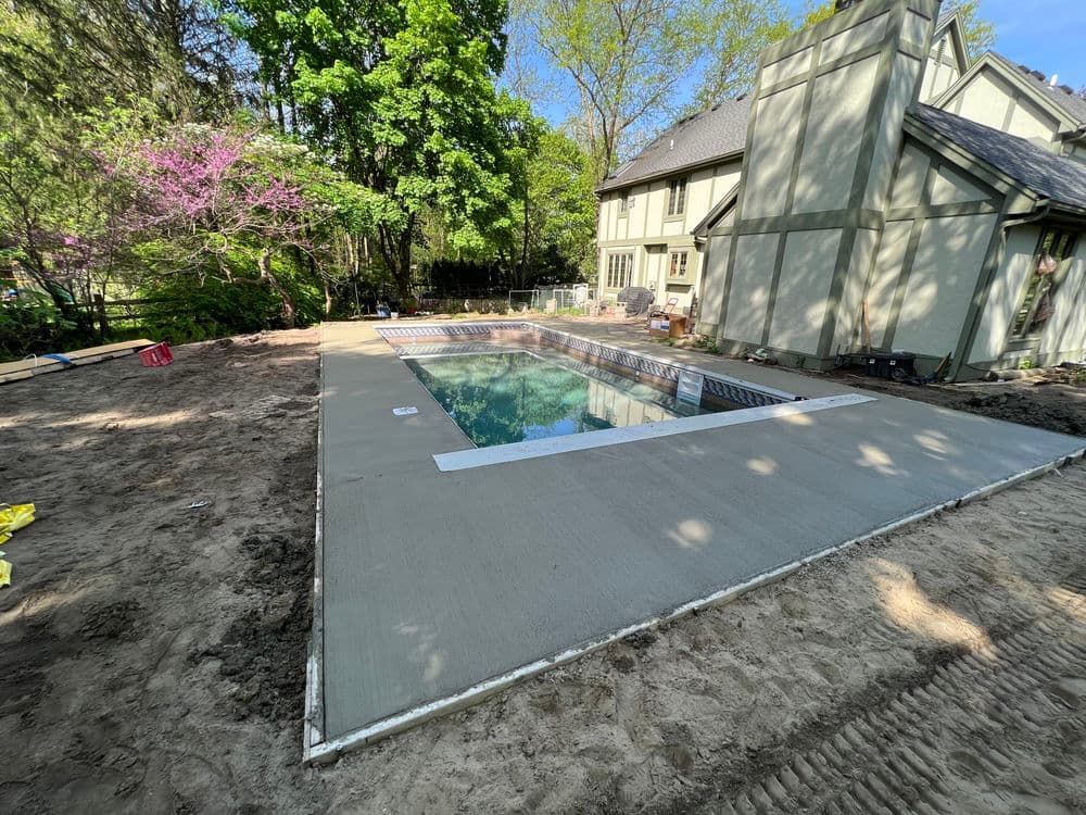 Newly installed concrete pool surround at a residential home under sunny skies and greenery.
