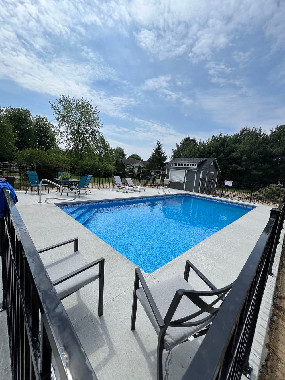 Outdoor swimming pool with lounge chairs, surrounded by greenery and a shed on a sunny day.