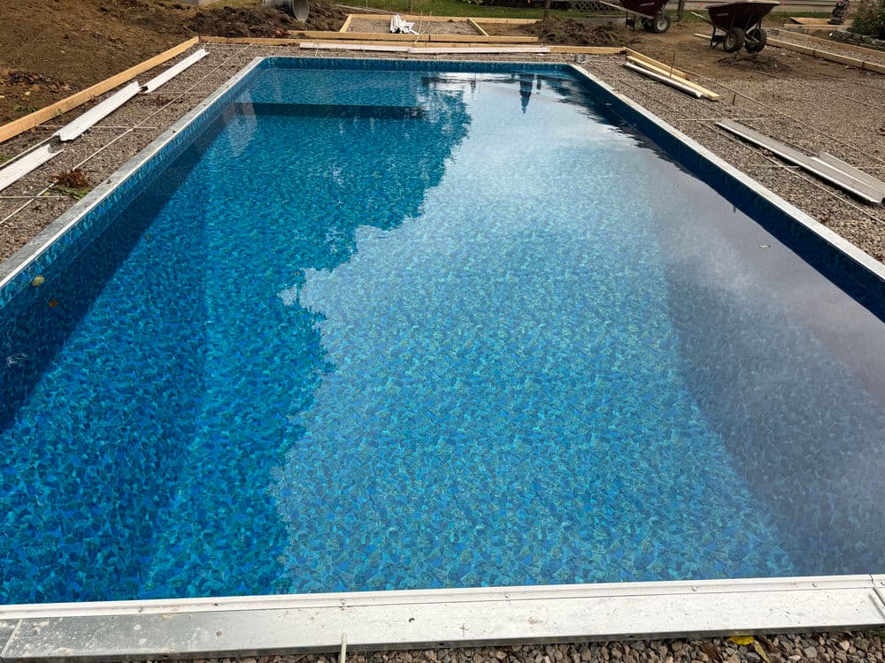 In-ground swimming pool under construction with clear blue water and gravel surrounding.
