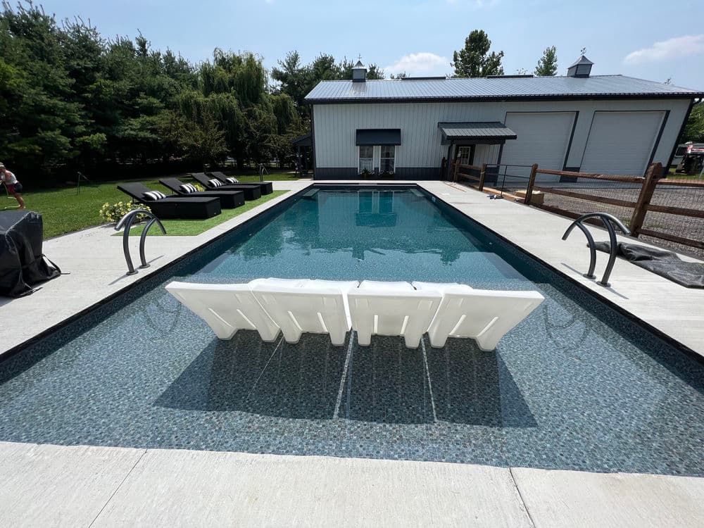 Modern swimming pool with lounge chairs, surrounded by greenery and a stylish building.