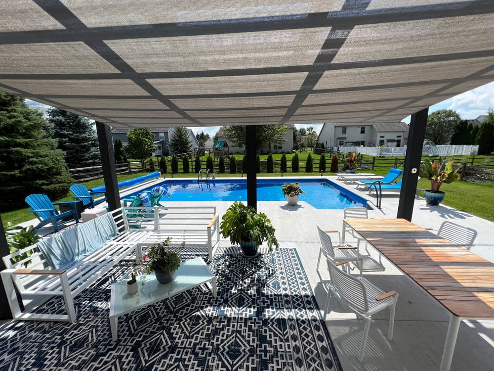 Modern outdoor patio with pool, shaded seating, and vibrant greenery, perfect for relaxation.
