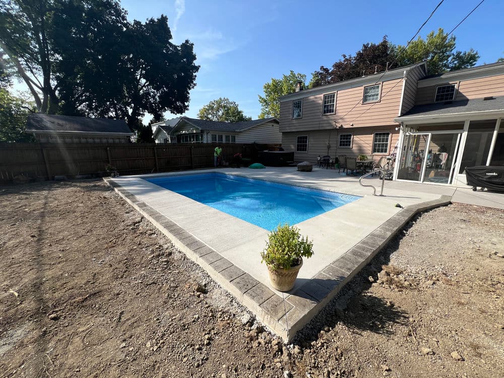 Newly built in-ground swimming pool with surrounding patio in a backyard setting.