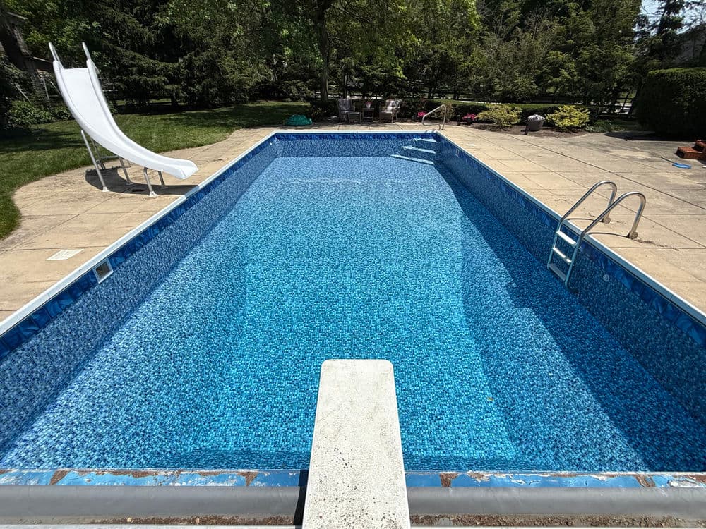 In-ground swimming pool with slide, diving board, and clear blue water on sunny day.