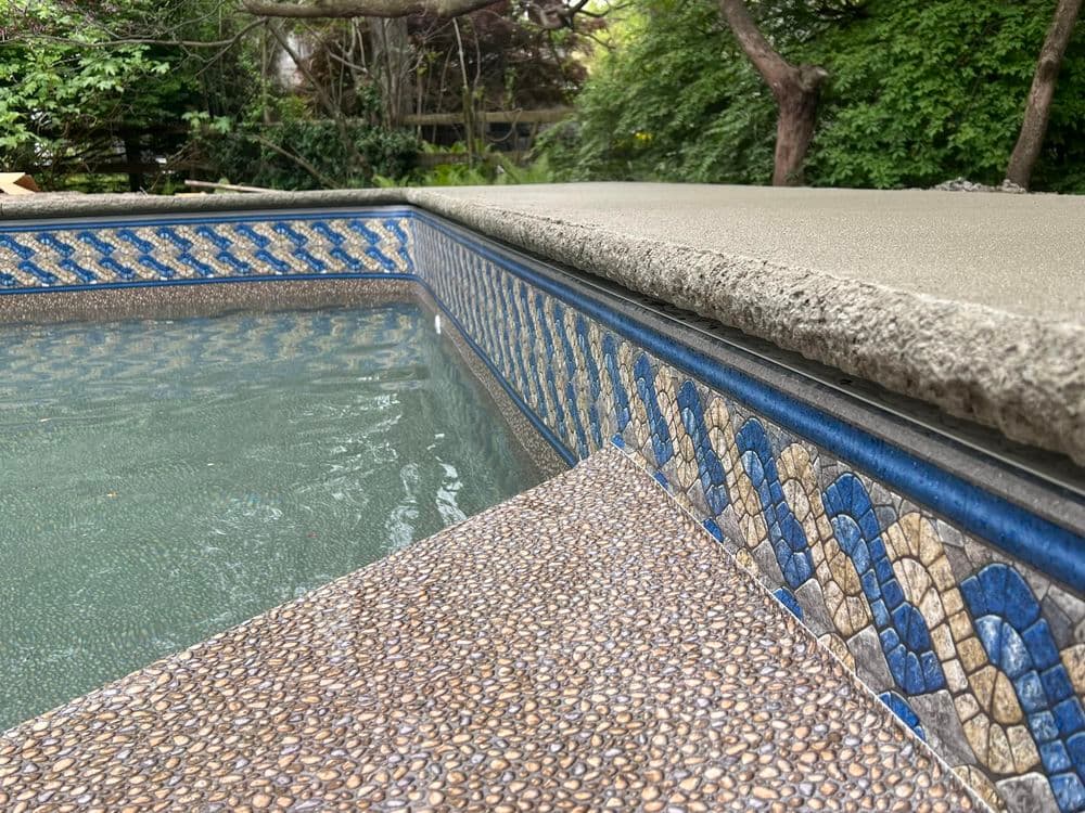 Close-up of a swimming pool edge with decorative tiles and textured concrete surface.